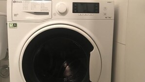 Una lavatrice a carica frontale con pannello di controllo digitale, attacco per tubo e manopola di regolazione.