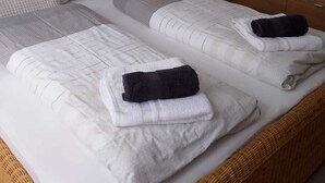 Un letto matrimoniale con biancheria da letto bianca e due asciugamani neri, un comodino con lampada, una cassettiera in legno e un quadro astratto appeso al muro.