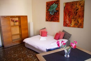 Ein Schlafzimmer mit einem Bett, einem Holzschrank, einem Tisch mit Blumen in einer Vase und zwei abstrakten Gemälden an der Wand.