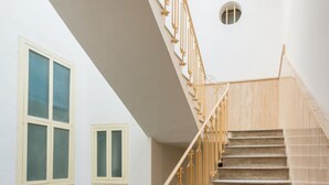 Una escalera con barandillas y peldaños de madera, un aplique de pared y dos ventanas con marcos blancos.