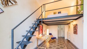 Una escalera conduce a un dormitorio en loft con una cama, una mesa con un florero y piso estampado.