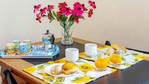 Una mesa de desayuno con un mantel individual estampado con flores, un jarrón de flores y una bandeja con tazas y pasteles.