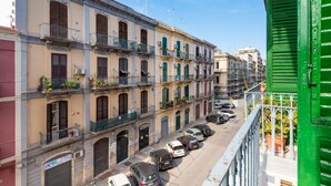 Un edificio de varios pisos con balcones, coches aparcados y un persiano verde.