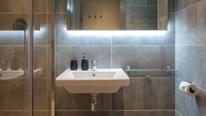 A modern bathroom with a glass shower enclosure, a white sink with black soap dispensers, and a toilet.