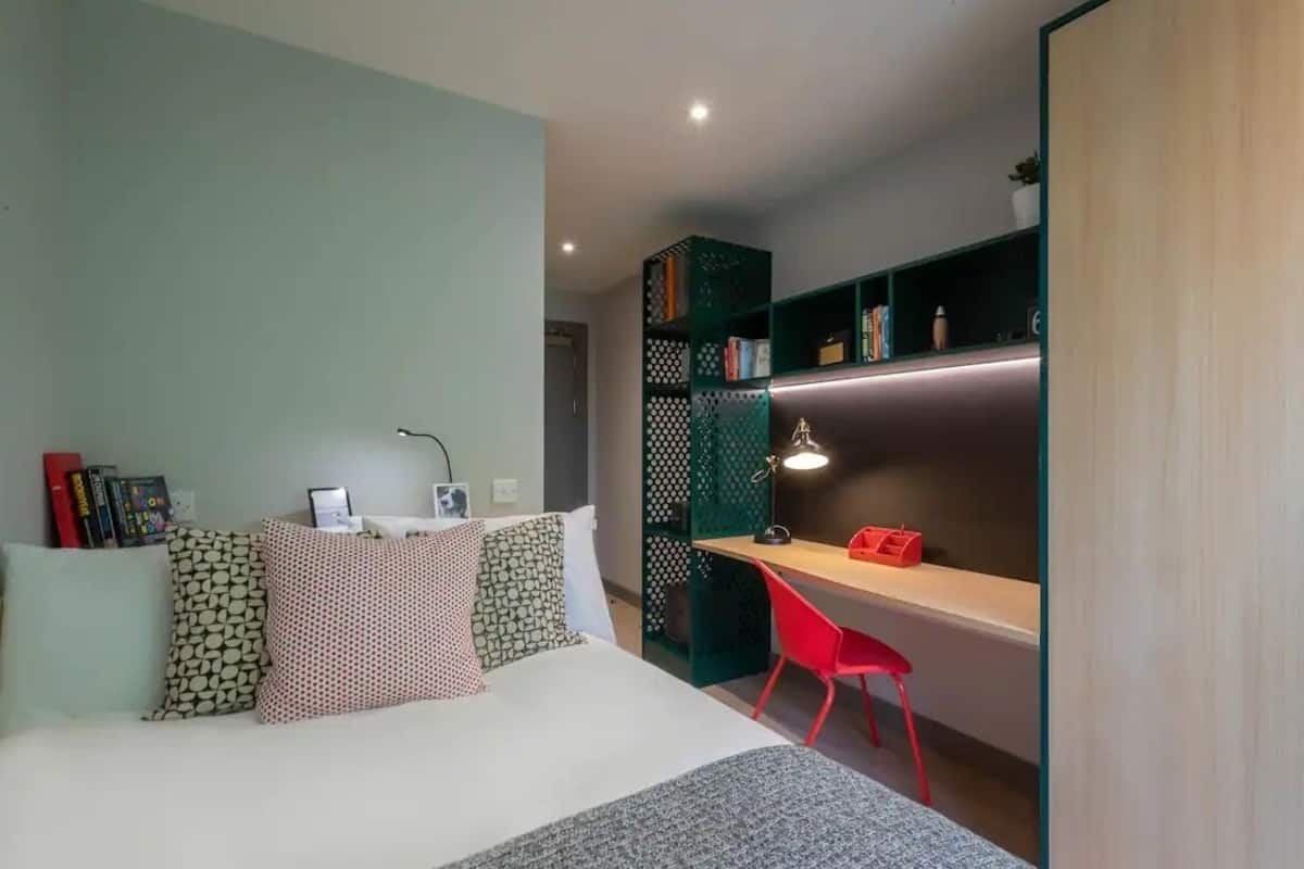 Een slaapkamer met een bed, bureau, stoel en een boekenkast.