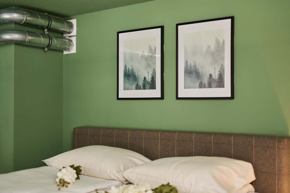 Un dormitorio con una cama, almohadas, un cabecero y dos cuadros en la pared.