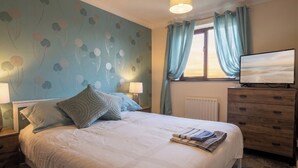 Un lit bien fait, avec des oreillers, une lampe de chevet, une commode et un téléviseur posé sur la commode.