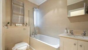 A bathroom with a bathtub, toilet, and vanity with a mirror. - Spacious 2 Bed Flat Near High Street Kensington (London)