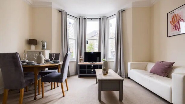 A living room with a dining area, a TV, and a white sofa. - Spacious 2 Bed Flat Near High Street Kensington (London)