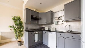 A compact kitchen with grey cabinets, a stove, oven, dishwasher, and a sink. - Spacious 2 Bed Flat Near High Street Kensington (London)