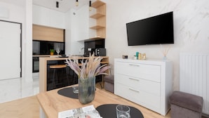 A modern living room with a wooden coffee table, a white cabinet, a flat-screen TV, and a kitchen area in the background. - Modern Apartment in Praga | Parking and Balcony (Warszawa)