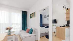 A modern, well-lit room with a sofa, a small table, and a bed. There is a TV mounted on the wall and a wooden desk. - Modern Apartment in Praga | Parking and Balcony (Warszawa)