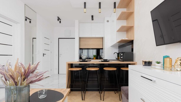 A modern kitchen with a central island, bar stools, and a flat-screen TV mounted on the wall. - Modern Apartment in Praga | Parking and Balcony (Warszawa)
