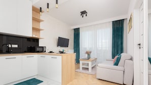 A modern living room with a sofa, a coffee table, and a TV. There is a kitchen area with cabinets and a microwave. - Modern Apartment in Praga | Parking and Balcony (Warszawa)