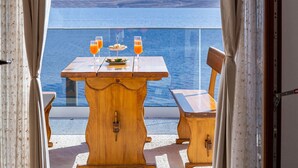 Ein Holztisch mit zwei Orangensaftgläsern und einer Speisenplatte auf einem Balkon mit Blick auf ein Gewässer.