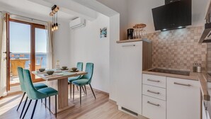 Eine moderne Küche mit weißen Schränken, einem schwarzen Fernseher über dem Herd und einem Essbereich mit türkisfarbenen Stühlen und einem Holztisch.