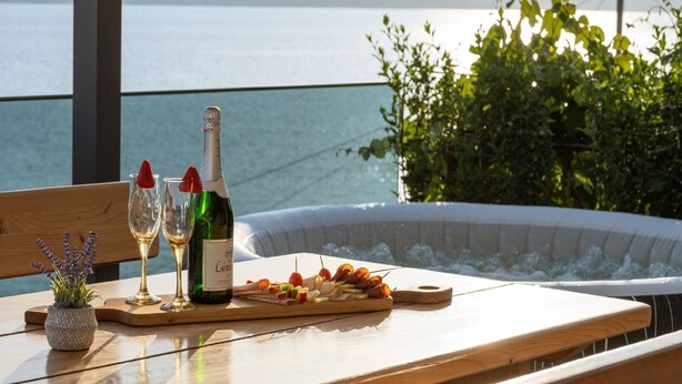Ein Tisch mit einer Weinflasche, zwei Gläsern, einer Auswahl an Vorspeisen und Blick auf das Meer.