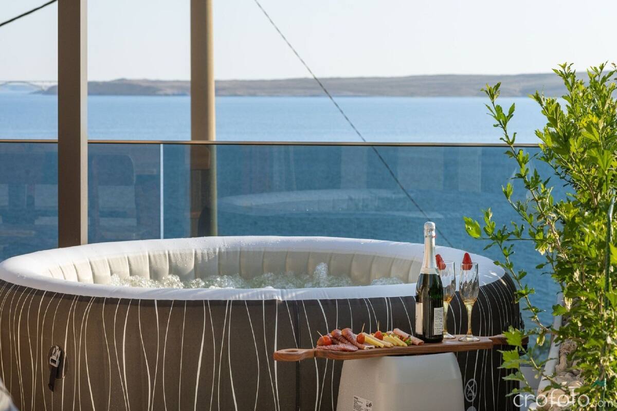 A hot tub with a wooden tray of snacks and drinks, overlooking a body of water.