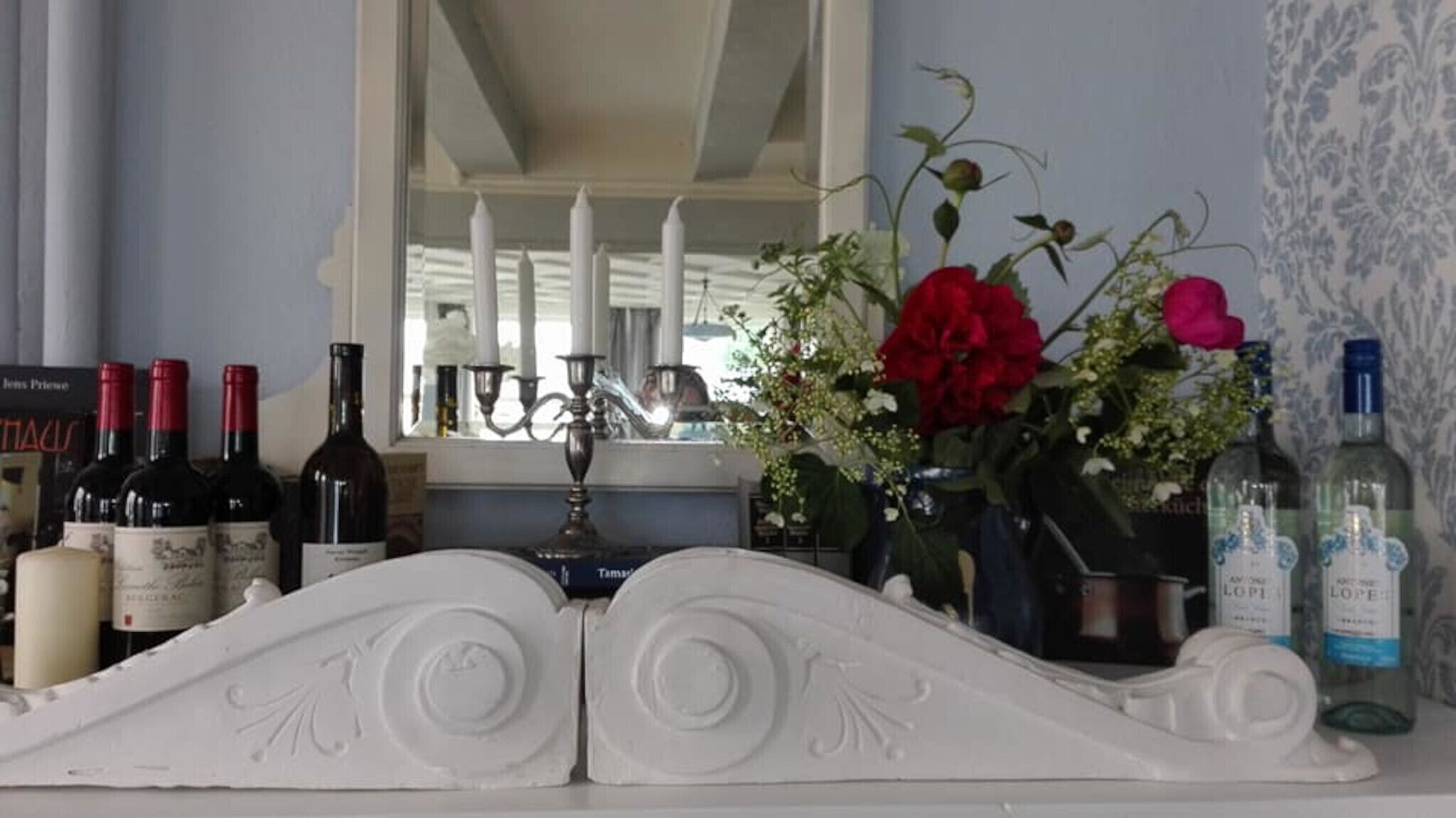 Zona de bar con botellas de licores, un florero con flores y un espejo que refleja la habitación.