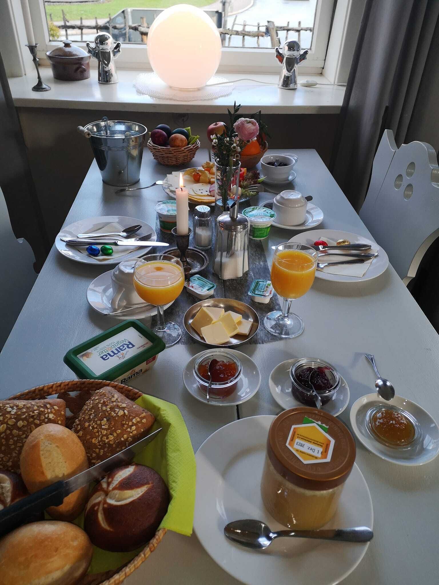 A breakfast table set with various food items, including bread, butter, jams, and a candle.