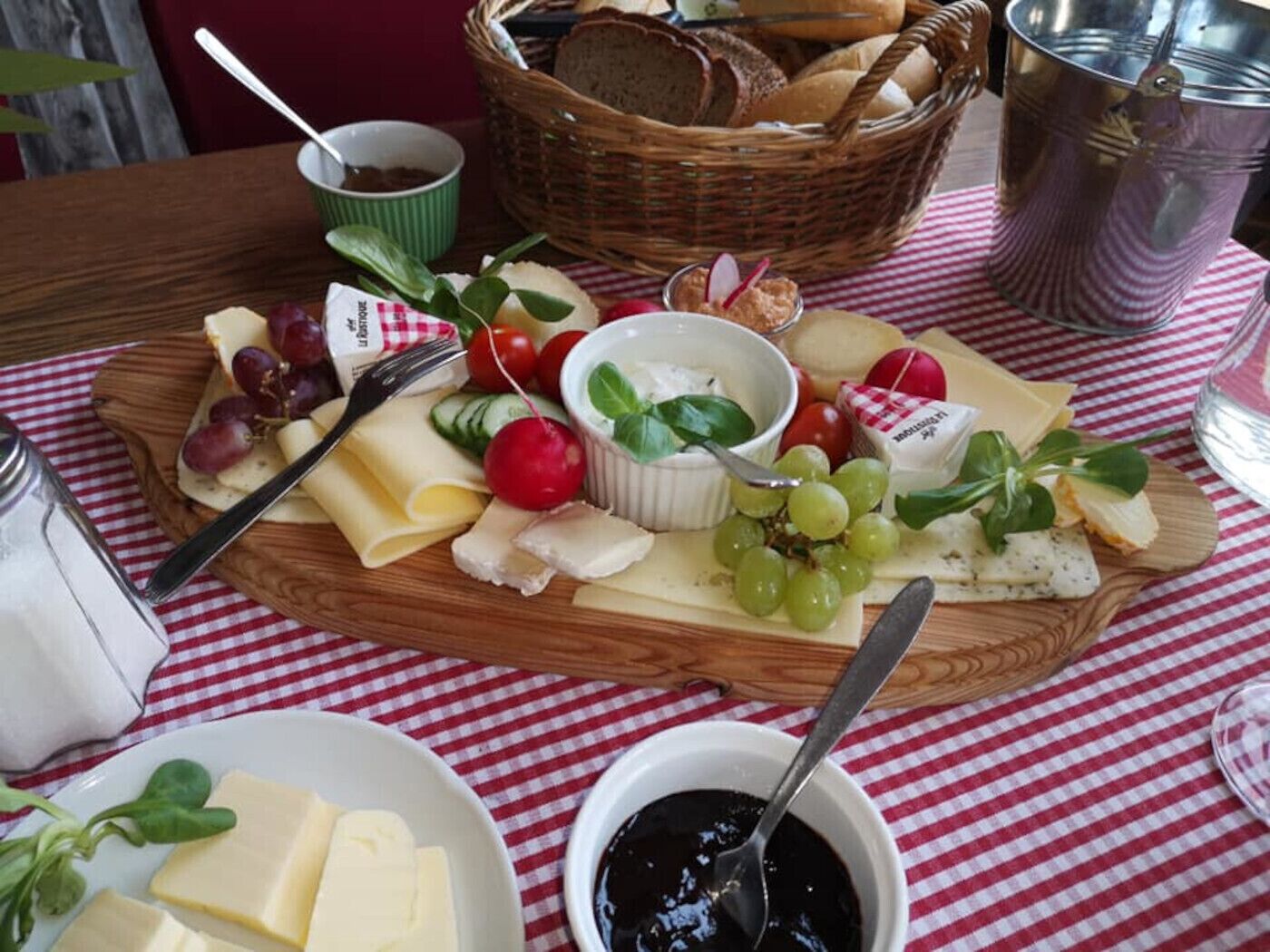 A cheese board with various cheeses, grapes, and vegetables on a checkered tablecloth.