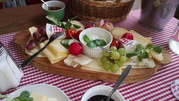 A cheese board with various cheeses, grapes, and vegetables on a checkered tablecloth.