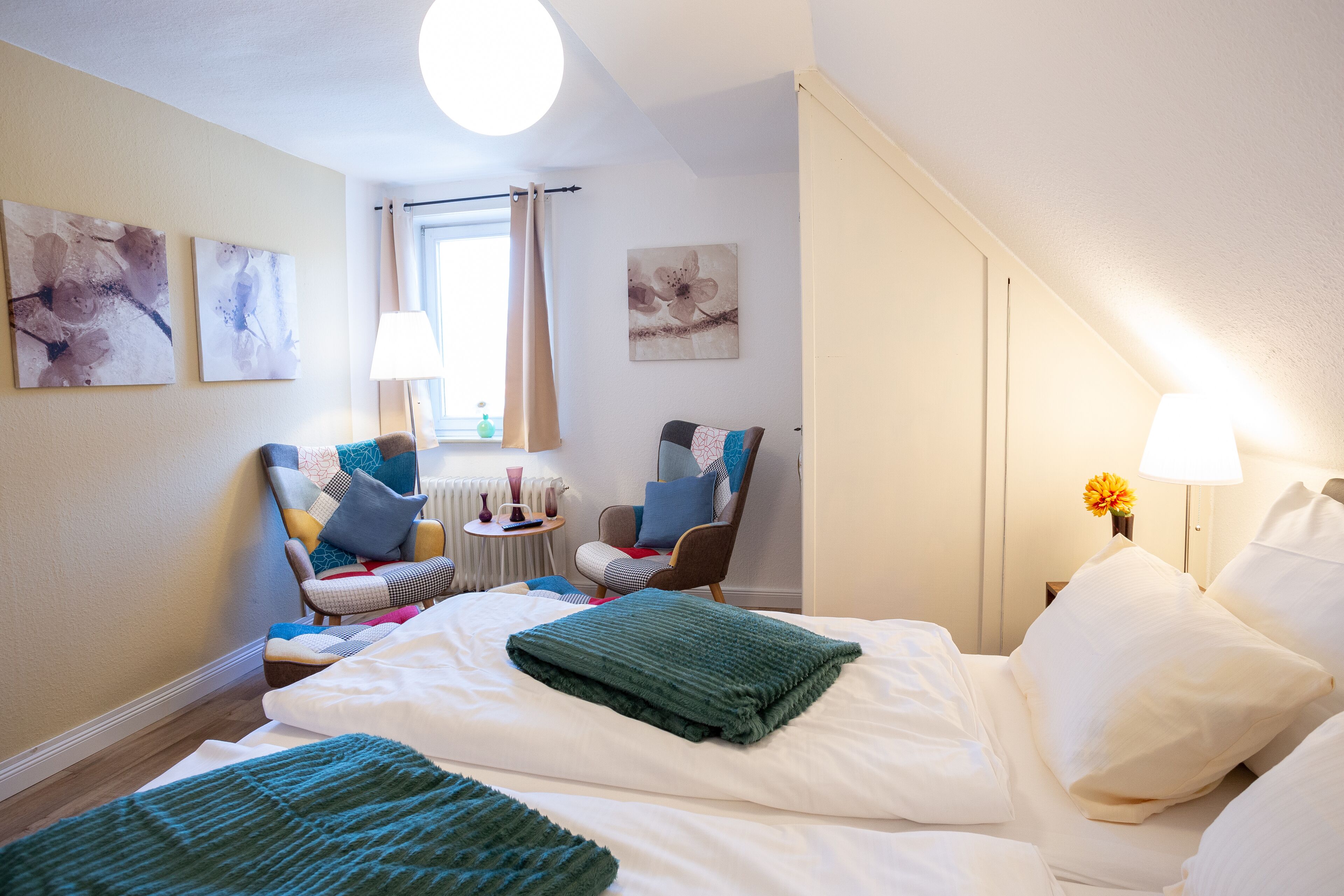Ein Hotelzimmer mit einem Bett, zwei Stühlen, einem Fenster mit Vorhängen und Bildern an den Wänden.