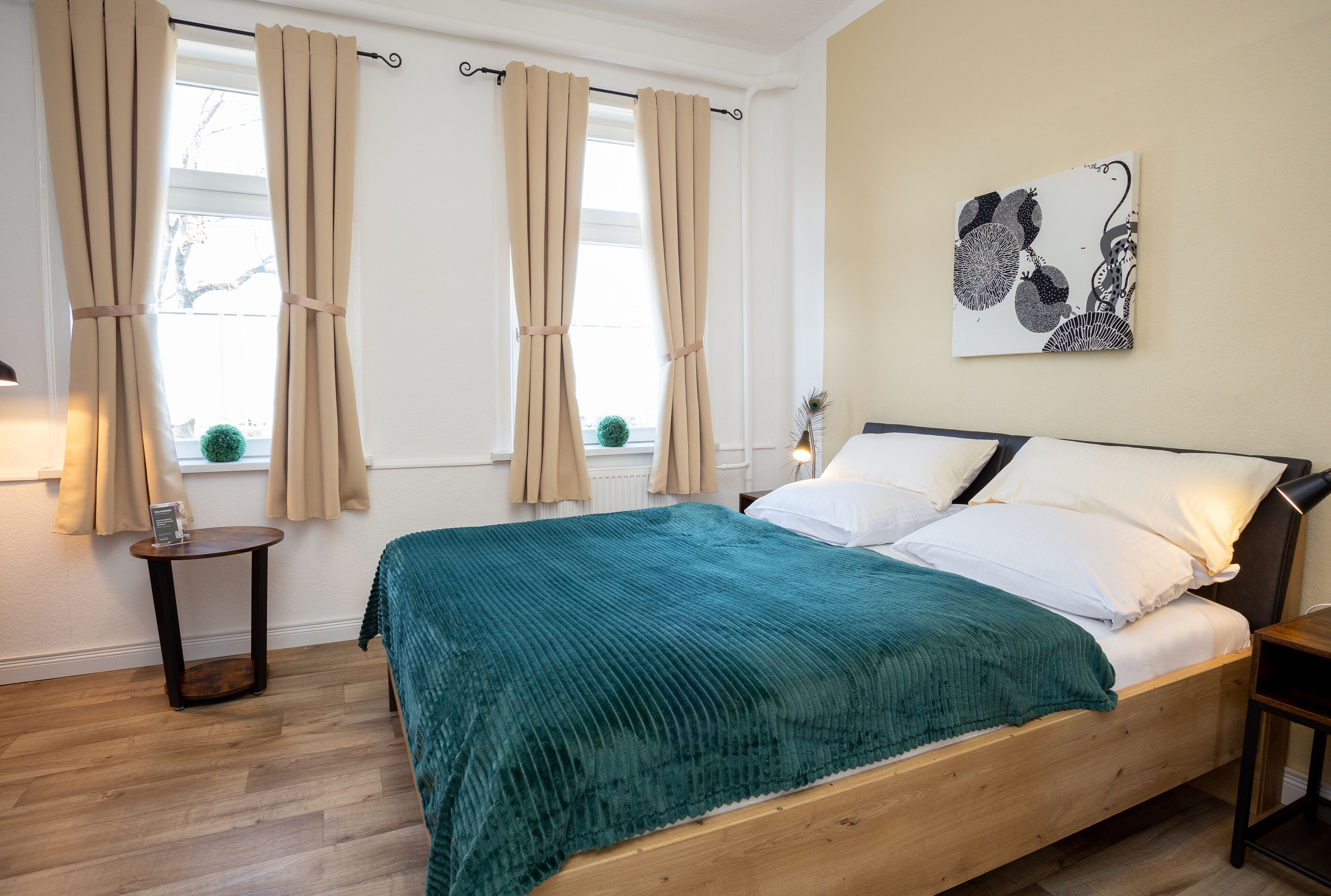 A neatly made bed with a teal blanket, a wooden headboard, and a wall-mounted artwork.
