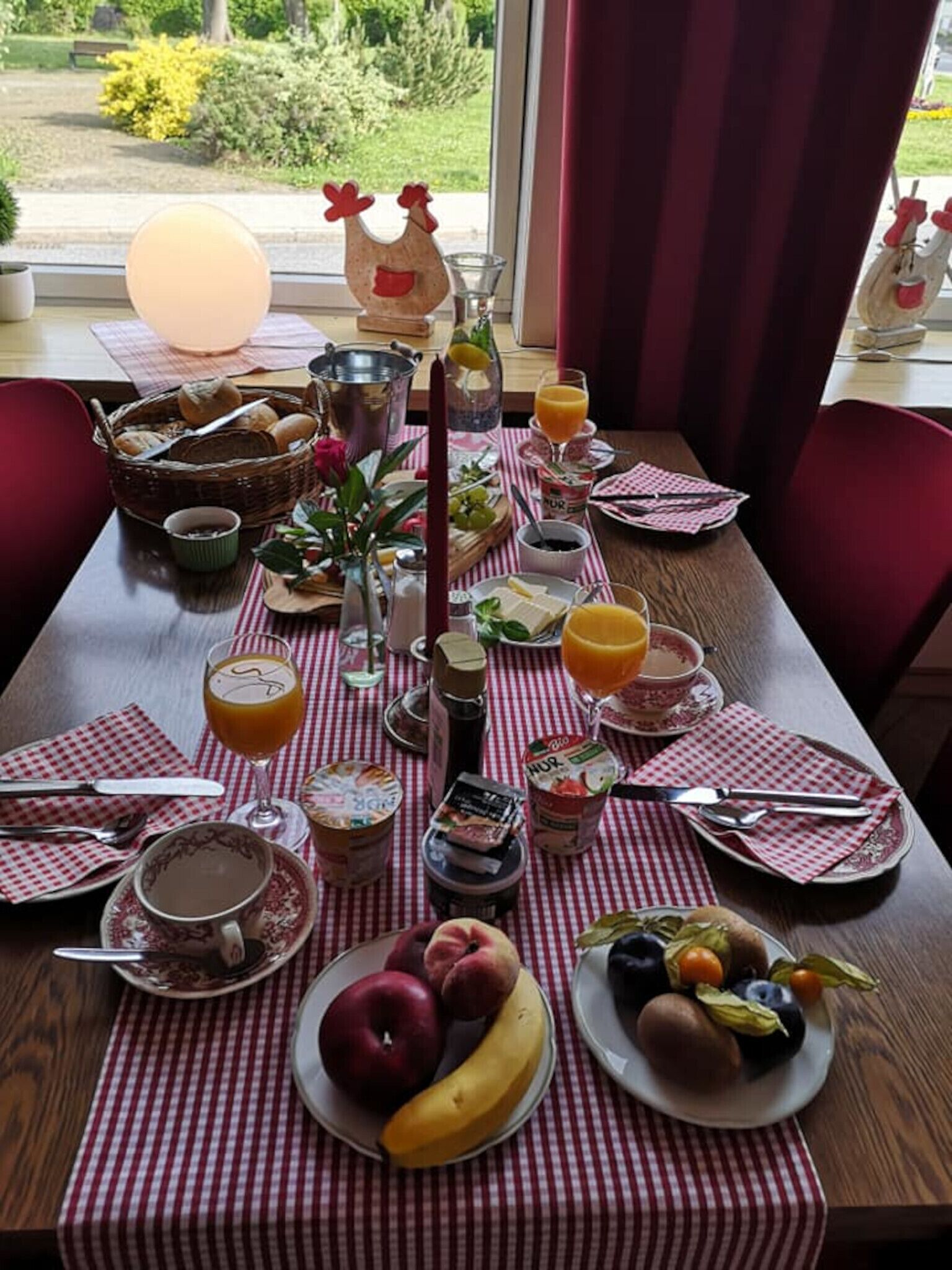Ein gedeckter Frühstückstisch mit verschiedenen Speisen, darunter Obst, Brot und Getränke, in einem Raum mit Blick aus dem Fenster.