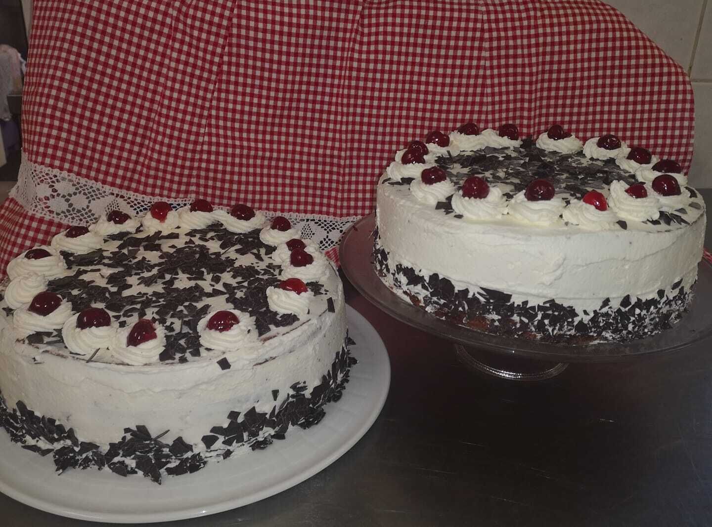 Deux gâteaux recouverts de glaçage blanc et décorés de cerises, posés sur une table.