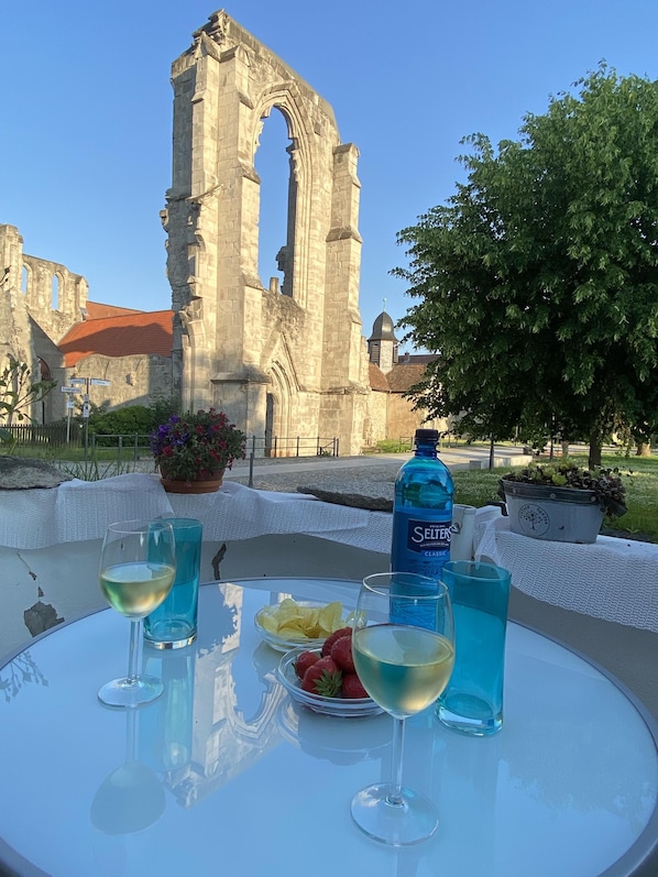 A table with a bottle of Seltzer, glasses of white wine, and a plate of strawberries, set against a backdrop of an ancient stone structure.