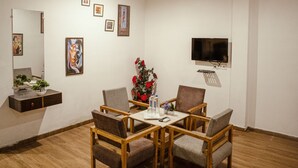 Un coin repas avec une table en bois et quatre chaises, un vase rempli de fleurs rouges et un téléviseur à écran plat fixé au mur.