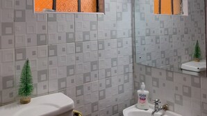 A bathroom with patterned tiles, a window with a black frame, a small Christmas tree, a toilet, a sink, and a mirror. - Stay.Plus Hill View Studio Apartment (Nairobi)