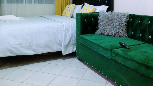 A bedroom with a bed, a green sofa, and a window with curtains. - Stay.Plus Hill View Studio Apartment (Nairobi)