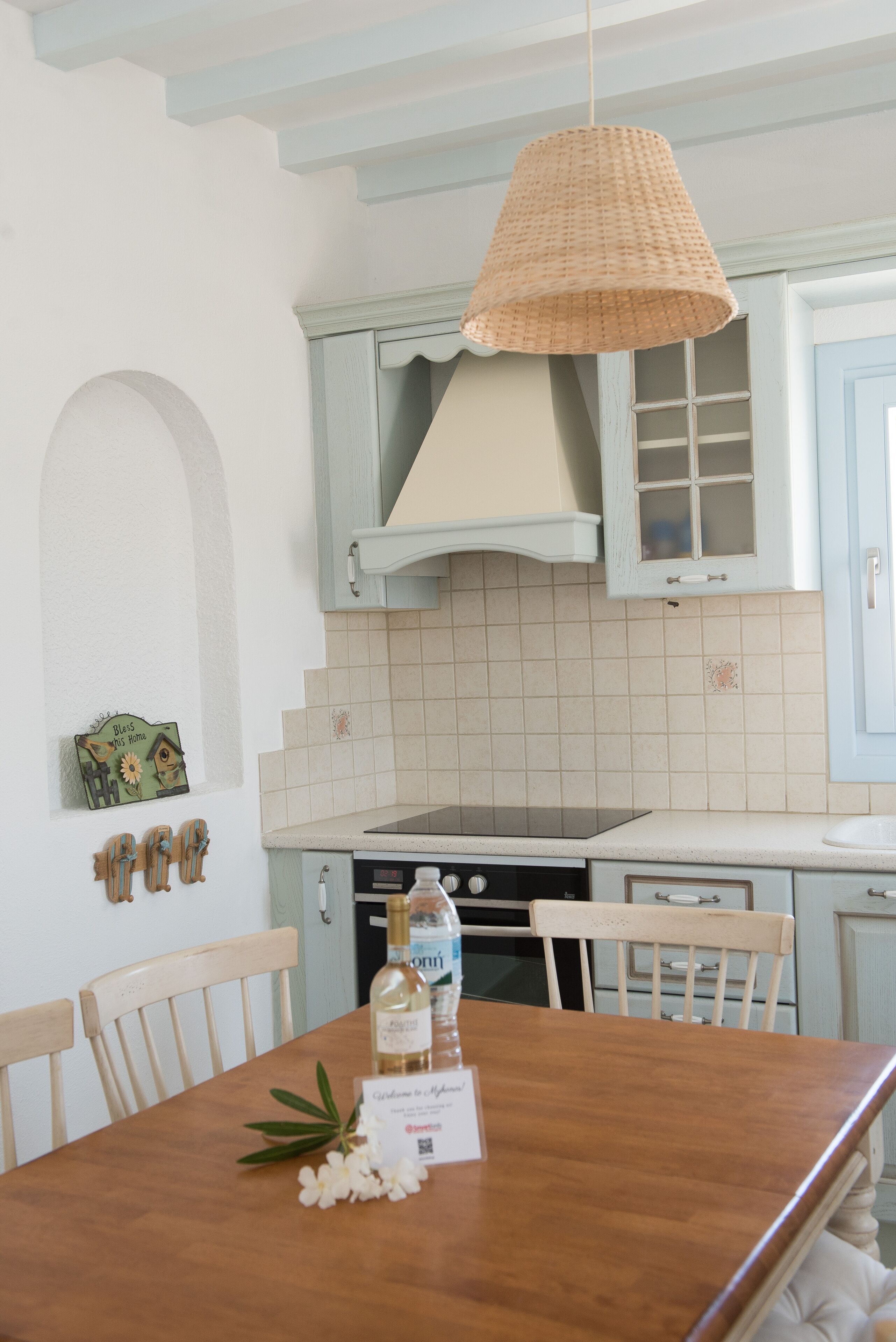 Una cocina con armarios azul claro, una lámpara colgante de fibras naturales y una mesa de comedor de madera con sillas.