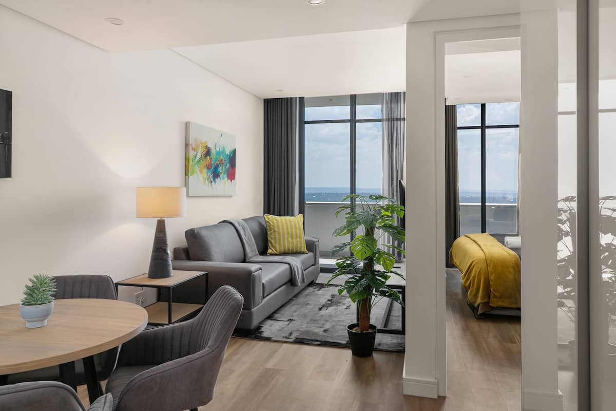 Un salon moderne avec un canapé gris, une table basse, une table à manger avec des chaises, une plante en pot et un tableau accroché au mur.
