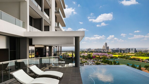 Un hôtel moderne doté d’une piscine à débordement sur le toit, d’une balustrade en verre et offrant une vue sur le paysage urbain et le parc.