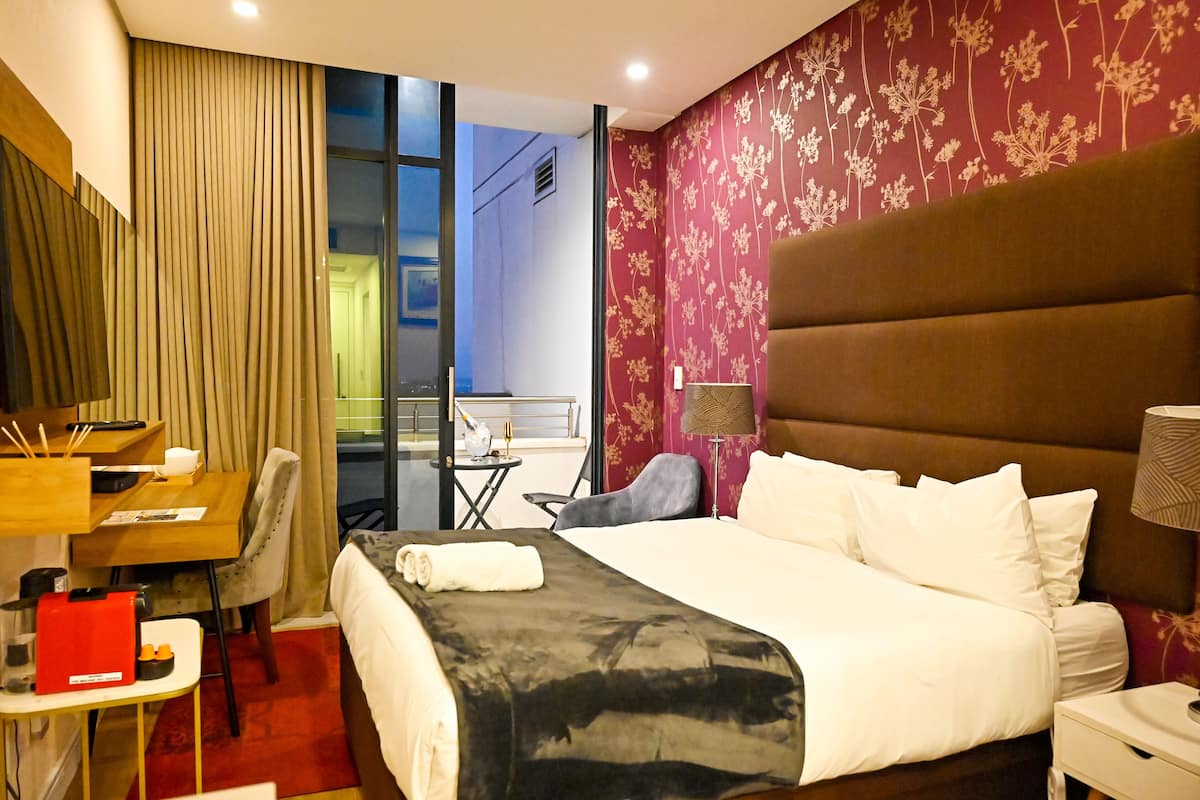 Une chambre d’hôtel avec un grand lit, un bureau avec une chaise, une petite table et une vue sur l’extérieur.