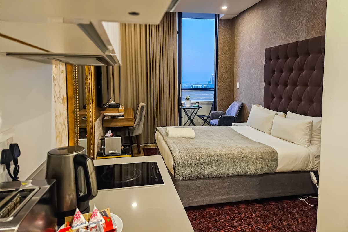 Une chambre d’hôtel avec un lit, un bureau avec un ordinateur, une chaise, une petite table et une vue sur la ville.