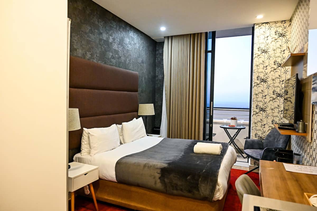 Une chambre d’hôtel avec un grand lit, un bureau, une chaise, une petite table et une vue sur l’océan.