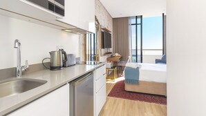 Une chambre d’hôtel moderne dotée d’un coin cuisine, d’un lit, d’une télévision et d’une grande fenêtre.