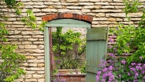 Un arc de pedra que dona pas a una zona de jardí amb una porta de fusta.