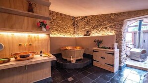 Una habitació d'spa amb un tocador de fusta, una banyera de coure gran i una paret de pedra.