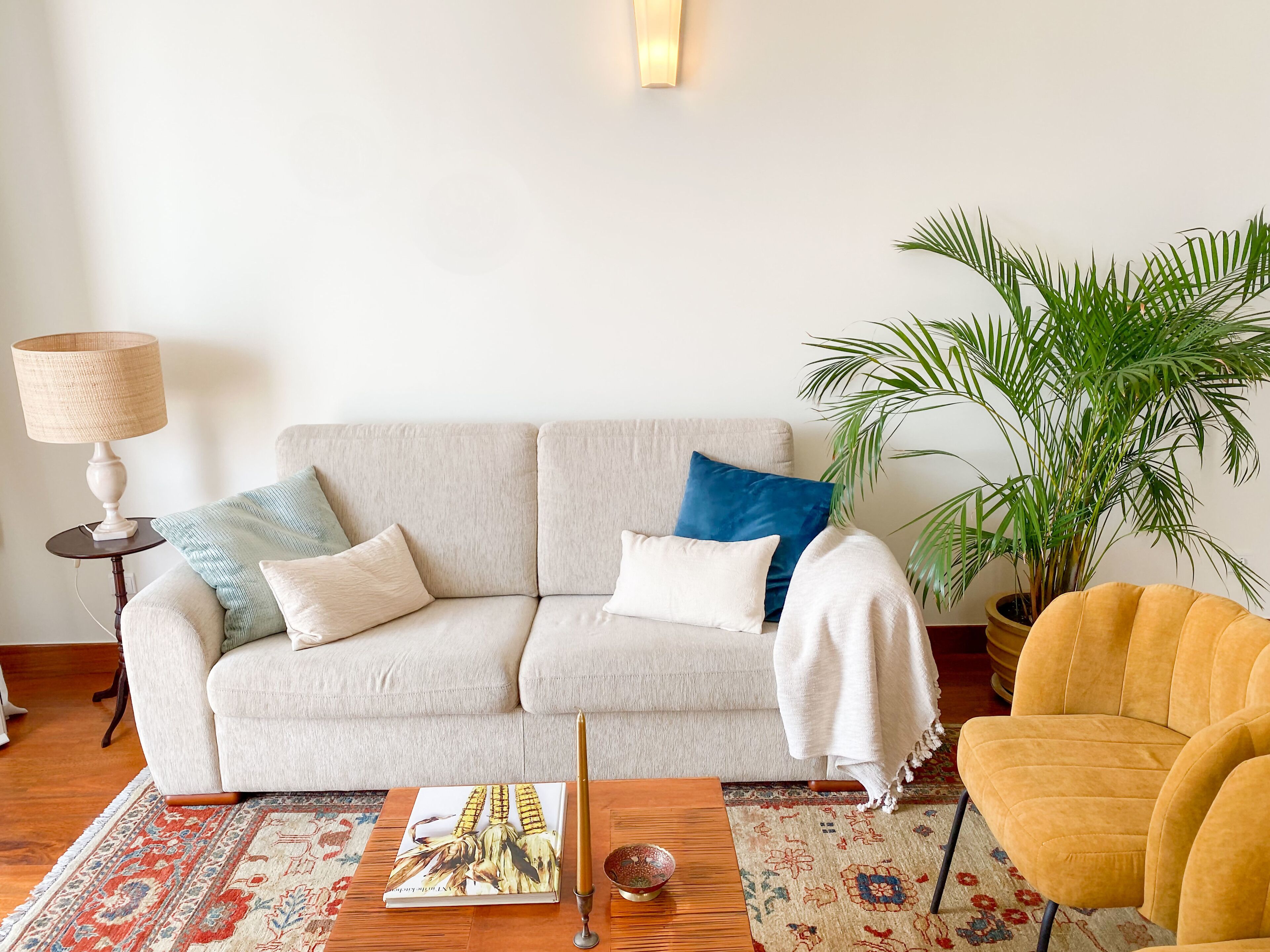 A living room with a sofa, a coffee table, a lamp, a potted plant, and a yellow armchair.