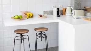 A modern kitchen with white tiles, a granite countertop, a coffee maker, a toaster, and two stools. - Madeira Precious Penthouse (Funchal)