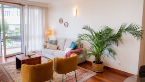A living room with a sofa, two armchairs, a coffee table, a potted plant, and a view through a sliding glass door. - Madeira Precious Penthouse (Funchal)
