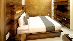 A modern bedroom with a wooden headboard, a flat-screen TV mounted on the wall, a ceiling fan, and a bedside table with a cup and tray. - Hotel SD Prime (Jaipur)