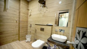 A modern bathroom with a wooden floor, a white toilet, a white sink, and a shower area. - Hotel SD Prime (Jaipur)