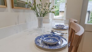 Een eettafel gedekt met blauwe en witte borden, een vaas met witte bloemen en een houten stoel.