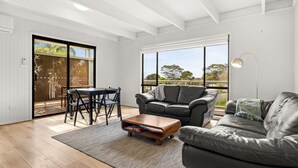 A modern living room with a sliding glass door leading to an outdoor area, a grey leather sofa, a wooden coffee table, and a dining table with chairs. - Hiddensee in Central Cowes (Cowes)